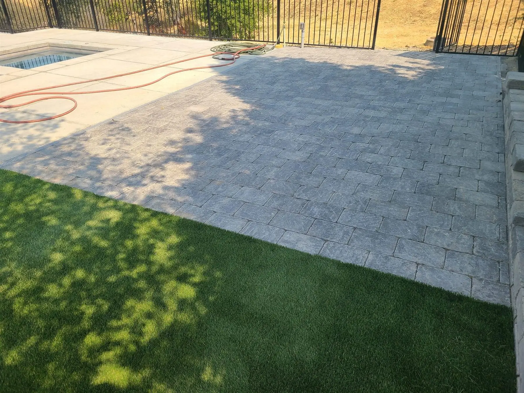 Artificial turf beside a finished paver patio and pool deck
